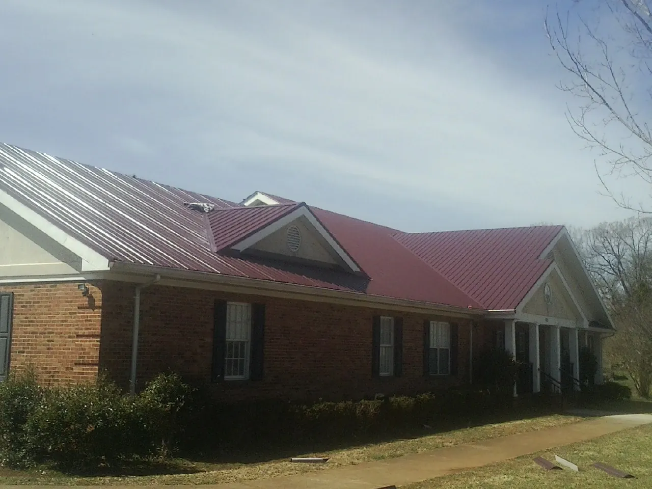 Red metal roof with gabled entries on a long brick building, from a Hail Damage Roof Repair job in Dudley