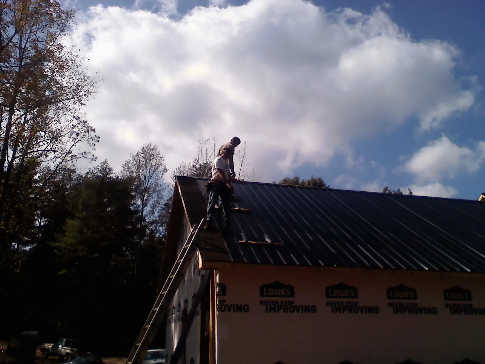 Roofer fastening dark metal panels high against a cloudy sky, from a Roof Inspection job in Dudley